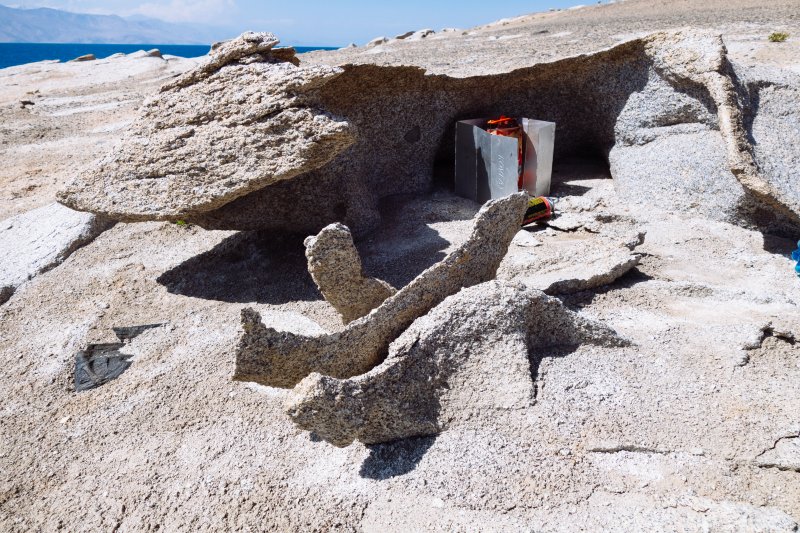 Как и в предыдущий день, буквально за
час ветер стал сильным, сохраняя направление – N. Непосредственно за мысом пространство
было защищено от волн, но южная оконечность невысокого галечного берега стала
накрываться набегающей волной почти до склона.
Прогулявшись на мыс и посмотрев
прибой с его северной стороны, принял решение ночевать здесь. По ходу движения
берег в обозримом пространстве обрывистый. На юге залива, куда идет волна, судя
по карте, должны быть мели - там заболоченная дельта реки Музкол. Вымокнуть при
высадке сильно не хотелось, это переводило бы уже ситуацию в борьбу за
выживание. Начиная с 17 часов здесь становится ощутимо холодно, приходится
надевать под мембранный костюм весь имеющийся полартек. Так еще до берега то
надо доплыть, серфинг на волне метровой высоты – развлечение не очень веселое,
при температуре воды 8 – 10 °С.
Правда и на берегу ситуация складывалась
так себе. Ровные площадки для установки палатки были только на верху мыса, там
нормально держались в грунте колышки, да и за камни можно зацепить оттяжки. Но
от ветра такой силы палатке могло очень поплохеть. На галечном берегу ровное
место под палатку есть, однако, во-первых сюда тоже прорывались порывы ветра
из-за мыса. Прорывались ударом, одним из которых перевернуло лежащую поперек
ветра байдарку, после чего ее пришлось догрузить камнями, для безопасности.
Во-вторых, колышки хоть и входят в мелкую гальку, но держат там крайне ненадежно.
А крупных камней, за которые можно было бы привязать веревки оттяжек, рядом
нет. Был еще и третий момент – если ветер поменяет направление на более
западный, есть риск, что волна начнет захлестывать гальку до самого обрыва и
подтопит палатку.
До темноты времени еще много, начал
эксперименты с палаткой. Попытка установить палатку на галечном берегу чуть не
привела к ее потере. Сильным ударом прорвавшегося из-за мыса порыва ветра,
палатку подкинуло в воздух, вырвав из гальки девять колышков, которые успел
закрепить. При этом одну дугу погнуло в двух местах. Палатку чудом успел
поймать, прыгнув за ней с берега в озеро. Хорошо, что на таком ветру быстро
просушить палатку и одежду не составило труда. Вопрос с ночевкой решился так –
из лежащей поперек ветра байдарки была сделана стенка, путем засыпания галькой щелей
между байдаркой и берегом. За байдарку закрепил веревкой угловые оттяжки одной
стороны внутренней палатки, в которую потом положил каремат, надувной коврик и
спальники. Дождя здесь не можно не опасаться, росы по утрам тоже нет. Тент
палатки нужен только от ветра. Оставалась угроза подмокания от волны, при
перемене направления ветра. Но мне повезло, переночевал нормально.
День 3 (16.08.2025)
15 км.
Проснулся в 6:00, позже чем вчера, однако
солнца еще нет – закрывает близко расположенный склон горы на полуострове. Без
солнца утром руки быстро замерзли, все работы пришлось выполнять в флисовых перчатках.
Поэтому провозился с завтраком и вышел на воду только в 9:03. Дул легкий встречный
ветерок, и я решил пойти метрах в семистах от берега, немного срезая залив.
Сегодня важно было добраться до строящейся охотничьей базы на юго-западном берегу
озера. Воды, пригодной для питья, осталось менее 3 литров. На базе, по словам
местных, дежурит сторож, у него можно раздобыть воды.
Когда стартовал, увидел на юге, над
снежными вершинами хребта Зартошкол, кучевые облака. Облака постепенно
приближались, одно из них закрыло солнце, и вода озера стала черной. Неожиданно
в 9:20, метрах в пятистах впереди, вода побелела. Только успел подумать – «это
что-то нехорошее», как шквал долетел до меня. Ладно хоть ветер встречный, он не
так опасен. Но стало жутко холодно, к тому же быстро промок от брызг, срываемых
ветром с пенных гребней моментально поднявшихся волн. Повернул налево, чтобы
легче было преодолевать ветер, и изо всех сил погреб к берегу.
В общем, когда в 9:35, проклиная свою
самоуверенность дошел до берега, то уже ощутимо замерз. Пристать удалось в бухточку,
отделенную с юга галечной косой от основной акватории, правда при этом сел на
мель, пересекая подводный вал у входа в бухту с севера. Быстро вылез, провел
байдарку до берега и вытащил ее на камни осыпи под обрывом. Стуча зубами от
холода, отцепил герму с сухой одеждой и полез с ней наверх.
Переодевание в полартек и мембранный
костюм, а также пара съеденных конфеток-халвы, сильно помогли. Осмотрелся, одел
ботинки и пошел по берегу на юго-запад, проверять воду в указанном на карте OSM в
паре километров отсюда ручье. Как и ожидалось – русло сухое. Прогулялся по нему
еще с километр вверх, до пересечения с дорогой, но результат тот же. Зато окончательно
согрелся. По наблюдениям, сделанным еще во время акклиматизационного выхода на
гору Уртабуз, вода здесь в это время года есть только в ручьях и речках,
текущих непосредственно от ледников или снежников. Да и то, до озера часто не
дотекает, уходит в песок.
Вернувшись к байдарке, взял бутылку с
питьевой водой, пакет с сухарями, спрятался от ветра за камень и начал размышлять.
Конечно, сильно удивило, что ветер начался с утра, а не с обеда, и не с севера,
как обычно, а с юго-запада. А может именно в этом все и дело. Пока надо было решать,
как двигаться дальше. Ветер то немного стихал, то вновь расходился не на шутку.
Со стартом были проблемы – вне бухты волной наплещет воды в байдарку, пока юбку
одеваю. А из бухты стартовать не получится, глубина при пересечении подводного
вала маловата, я прошел ногами и все промерил. В итоге - продолжил сидеть за камнем,
благо тучи разошлись, на солнце стало тепло.
К обеду отметил особенность ветра,
что каждые минут десять он утихает на минуту, потом возобновляется с новой
силой. Решил использовать этот промежуток для старта. Оставаться здесь не
хотелось, пришлось бы сильно ужаться в потреблении воды, и не факт, что завтра
погода будет лучше. Вообще без питьевой воды в пустыне довольно грустно.
Сумел осуществить задуманный старт в
14:39 и пошел вдоль берега против ветра. Скорость, конечно, раза в полтора-два
меньше, но продвижение шло, мне не так-то и много до базы. Аккуратно, чтоб не
сесть на мель, дошел до острова, и спрятавшись за ним от ветра и волн добрался
до его западного края, а затем перегреб залив на западный берег. В очередной
раз констатировал неточность карты у меня в GPS, но генштабовская километровка была
еще хуже. В общем линия берега, где полого, сильно не совпадает с имеющимися
картами, местами разница в километры! Растет уровень озера, а также оттаивают
берега из вечной мерзлоты.
Двигаясь теперь по ветру
вдоль западного берега, пошел ко входу в залив, рядом с которым строят
охотничью базу. Глубины здесь маленькие, поэтому волна сзади была небольшая, несмотря
на сильный ветер. Достаточно безопасно серфил, рассматривая находившиеся на
левом берегу диковинные формы рельефа, последствия выветривания. Они
представляли из себя маленькие холмы, высотой 10-20 метров, с очень крутыми,
обточенными ветром краями, и казались какими-то застывшими сказочными чудищами.
В заливе ветер и волна были уже сбоку, слева, но терпеть оставалось не долго.
Мокрый от брызг в 16:40 вылез на подзаболоченный берег, максимально близко к видневшимся
метрах в трехстах юго-западнее строениям. Как и в предыдущий день, буквально за
час ветер стал сильным, сохраняя направление – N. Непосредственно за мысом пространство
было защищено от волн, но южная оконечность невысокого галечного берега стала
накрываться набегающей волной почти до склона.
Прогулявшись на мыс и посмотрев
прибой с его северной стороны, принял решение ночевать здесь. По ходу движения
берег в обозримом пространстве обрывистый. На юге залива, куда идет волна, судя
по карте, должны быть мели - там заболоченная дельта реки Музкол. Вымокнуть при
высадке сильно не хотелось, это переводило бы уже ситуацию в борьбу за
выживание. Начиная с 17 часов здесь становится ощутимо холодно, приходится
надевать под мембранный костюм весь имеющийся полартек. Так еще до берега то
надо доплыть, серфинг на волне метровой высоты – развлечение не очень веселое,
при температуре воды 8 – 10 °С.
Правда и на берегу ситуация складывалась
так себе. Ровные площадки для установки палатки были только на верху мыса, там
нормально держались в грунте колышки, да и за камни можно зацепить оттяжки. Но
от ветра такой силы палатке могло очень поплохеть. На галечном берегу ровное
место под палатку есть, однако, во-первых сюда тоже прорывались порывы ветра
из-за мыса. Прорывались ударом, одним из которых перевернуло лежащую поперек
ветра байдарку, после чего ее пришлось догрузить камнями, для безопасности.
Во-вторых, колышки хоть и входят в мелкую гальку, но держат там крайне ненадежно.
А крупных камней, за которые можно было бы привязать веревки оттяжек, рядом
нет. Был еще и третий момент – если ветер поменяет направление на более
западный, есть риск, что волна начнет захлестывать гальку до самого обрыва и
подтопит палатку.
До темноты времени еще много, начал
эксперименты с палаткой. Попытка установить палатку на галечном берегу чуть не
привела к ее потере. Сильным ударом прорвавшегося из-за мыса порыва ветра,
палатку подкинуло в воздух, вырвав из гальки девять колышков, которые успел
закрепить. При этом одну дугу погнуло в двух местах. Палатку чудом успел
поймать, прыгнув за ней с берега в озеро. Хорошо, что на таком ветру быстро
просушить палатку и одежду не составило труда. Вопрос с ночевкой решился так –
из лежащей поперек ветра байдарки была сделана стенка, путем засыпания галькой щелей
между байдаркой и берегом. За байдарку закрепил веревкой угловые оттяжки одной
стороны внутренней палатки, в которую потом положил каремат, надувной коврик и
спальники. Дождя здесь не можно не опасаться, росы по утрам тоже нет. Тент
палатки нужен только от ветра. Оставалась угроза подмокания от волны, при
перемене направления ветра. Но мне повезло, переночевал нормально.
День 3 (16.08.2025)
15 км.
Проснулся в 6:00, позже чем вчера, однако
солнца еще нет – закрывает близко расположенный склон горы на полуострове. Без
солнца утром руки быстро замерзли, все работы пришлось выполнять в флисовых перчатках.
Поэтому провозился с завтраком и вышел на воду только в 9:03. Дул легкий встречный
ветерок, и я решил пойти метрах в семистах от берега, немного срезая залив.
Сегодня важно было добраться до строящейся охотничьей базы на юго-западном берегу
озера. Воды, пригодной для питья, осталось менее 3 литров. На базе, по словам
местных, дежурит сторож, у него можно раздобыть воды.
Когда стартовал, увидел на юге, над
снежными вершинами хребта Зартошкол, кучевые облака. Облака постепенно
приближались, одно из них закрыло солнце, и вода озера стала черной. Неожиданно
в 9:20, метрах в пятистах впереди, вода побелела. Только успел подумать – «это
что-то нехорошее», как шквал долетел до меня. Ладно хоть ветер встречный, он не
так опасен. Но стало жутко холодно, к тому же быстро промок от брызг, срываемых
ветром с пенных гребней моментально поднявшихся волн. Повернул налево, чтобы
легче было преодолевать ветер, и изо всех сил погреб к берегу.
В общем, когда в 9:35, проклиная свою
самоуверенность дошел до берега, то уже ощутимо замерз. Пристать удалось в бухточку,
отделенную с юга галечной косой от основной акватории, правда при этом сел на
мель, пересекая подводный вал у входа в бухту с севера. Быстро вылез, провел
байдарку до берега и вытащил ее на камни осыпи под обрывом. Стуча зубами от
холода, отцепил герму с сухой одеждой и полез с ней наверх.
Переодевание в полартек и мембранный
костюм, а также пара съеденных конфеток-халвы, сильно помогли. Осмотрелся, одел
ботинки и пошел по берегу на юго-запад, проверять воду в указанном на карте OSM в
паре километров отсюда ручье. Как и ожидалось – русло сухое. Прогулялся по нему
еще с километр вверх, до пересечения с дорогой, но результат тот же. Зато окончательно
согрелся. По наблюдениям, сделанным еще во время акклиматизационного выхода на
гору Уртабуз, вода здесь в это время года есть только в ручьях и речках,
текущих непосредственно от ледников или снежников. Да и то, до озера часто не
дотекает, уходит в песок.
Вернувшись к байдарке, взял бутылку с
питьевой водой, пакет с сухарями, спрятался от ветра за камень и начал размышлять.
Конечно, сильно удивило, что ветер начался с утра, а не с обеда, и не с севера,
как обычно, а с юго-запада. А может именно в этом все и дело. Пока надо было решать,
как двигаться дальше. Ветер то немного стихал, то вновь расходился не на шутку.
Со стартом были проблемы – вне бухты волной наплещет воды в байдарку, пока юбку
одеваю. А из бухты стартовать не получится, глубина при пересечении подводного
вала маловата, я прошел ногами и все промерил. В итоге - продолжил сидеть за камнем,
благо тучи разошлись, на солнце стало тепло.
К обеду отметил особенность ветра,
что каждые минут десять он утихает на минуту, потом возобновляется с новой
силой. Решил использовать этот промежуток для старта. Оставаться здесь не
хотелось, пришлось бы сильно ужаться в потреблении воды, и не факт, что завтра
погода будет лучше. Вообще без питьевой воды в пустыне довольно грустно.
Сумел осуществить задуманный старт в
14:39 и пошел вдоль берега против ветра. Скорость, конечно, раза в полтора-два
меньше, но продвижение шло, мне не так-то и много до базы. Аккуратно, чтоб не
сесть на мель, дошел до острова, и спрятавшись за ним от ветра и волн добрался
до его западного края, а затем перегреб залив на западный берег. В очередной
раз констатировал неточность карты у меня в GPS, но генштабовская километровка была
еще хуже. В общем линия берега, где полого, сильно не совпадает с имеющимися
картами, местами разница в километры! Растет уровень озера, а также оттаивают
берега из вечной мерзлоты.
Двигаясь теперь по ветру
вдоль западного берега, пошел ко входу в залив, рядом с которым строят
охотничью базу. Глубины здесь маленькие, поэтому волна сзади была небольшая, несмотря
на сильный ветер. Достаточно безопасно серфил, рассматривая находившиеся на
левом берегу диковинные формы рельефа, последствия выветривания. Они
представляли из себя маленькие холмы, высотой 10-20 метров, с очень крутыми,
обточенными ветром краями, и казались какими-то застывшими сказочными чудищами.
В заливе ветер и волна были уже сбоку, слева, но терпеть оставалось не долго.
Мокрый от брызг в 16:40 вылез на подзаболоченный берег, максимально близко к видневшимся
метрах в трехстах юго-западнее строениям.